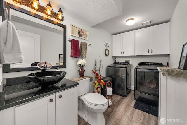 bathroom with toilet, a textured ceiling, wood finished floors, washing machine and dryer, and vanity