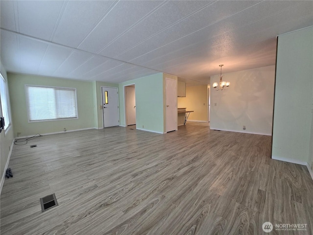 unfurnished living room with visible vents, baseboards, an inviting chandelier, and wood finished floors