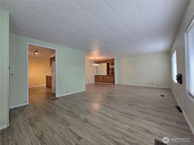 unfurnished living room with a notable chandelier, baseboards, and wood finished floors