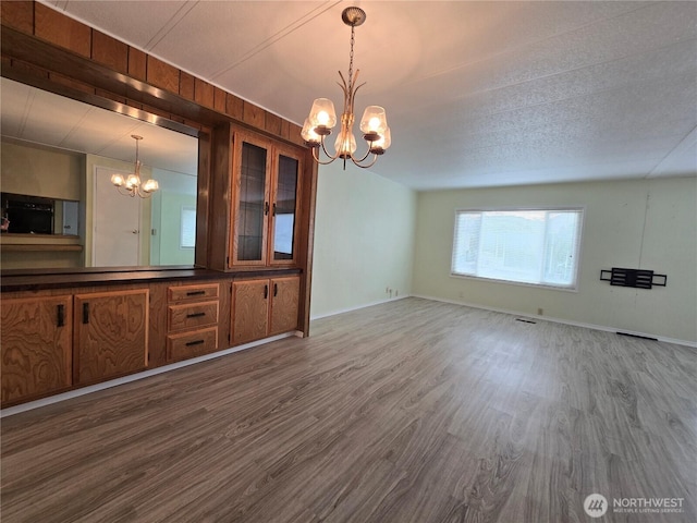 unfurnished dining area with visible vents, wood finished floors, baseboards, and a chandelier