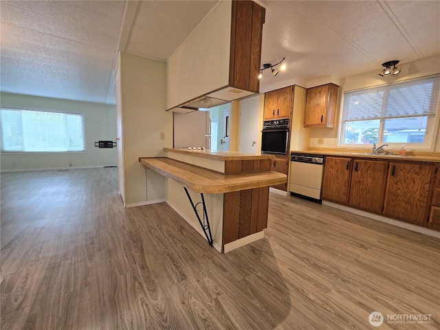 kitchen featuring black oven, light wood-style floors, white dishwasher, and a textured ceiling