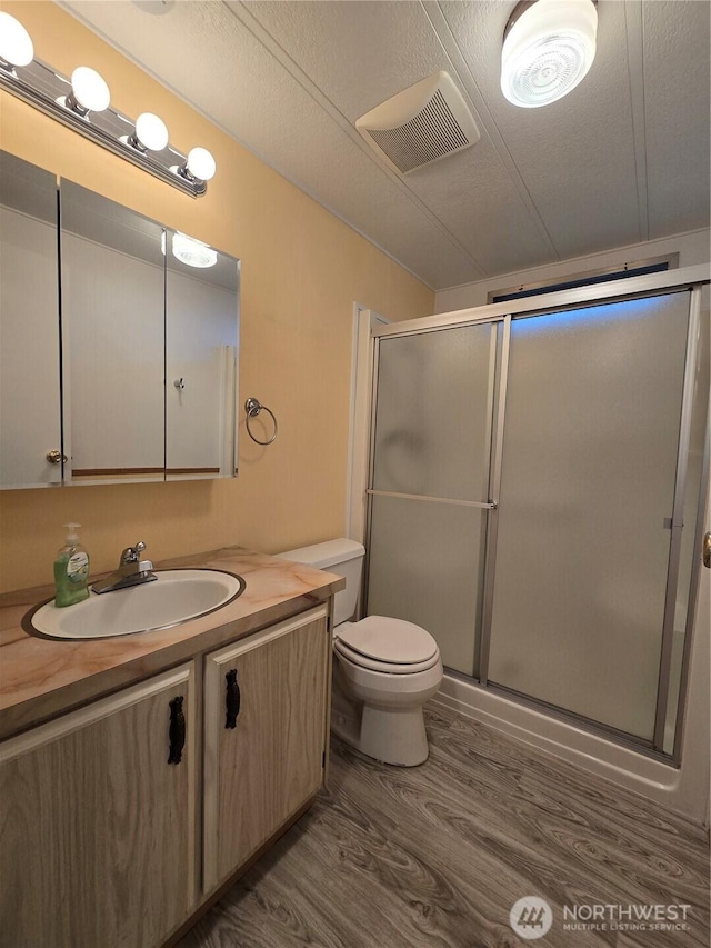 full bathroom with vanity, a shower stall, wood finished floors, and visible vents