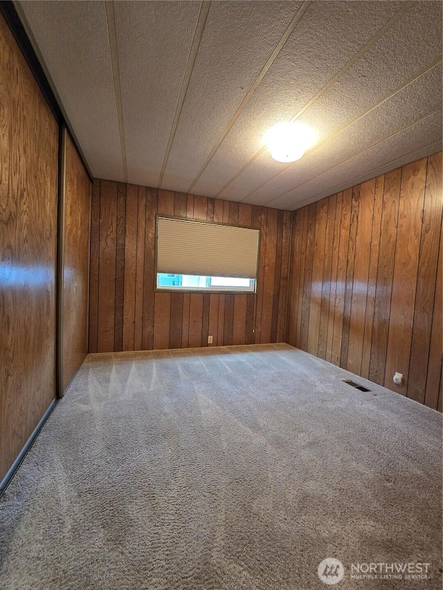 carpeted empty room with visible vents and wood walls