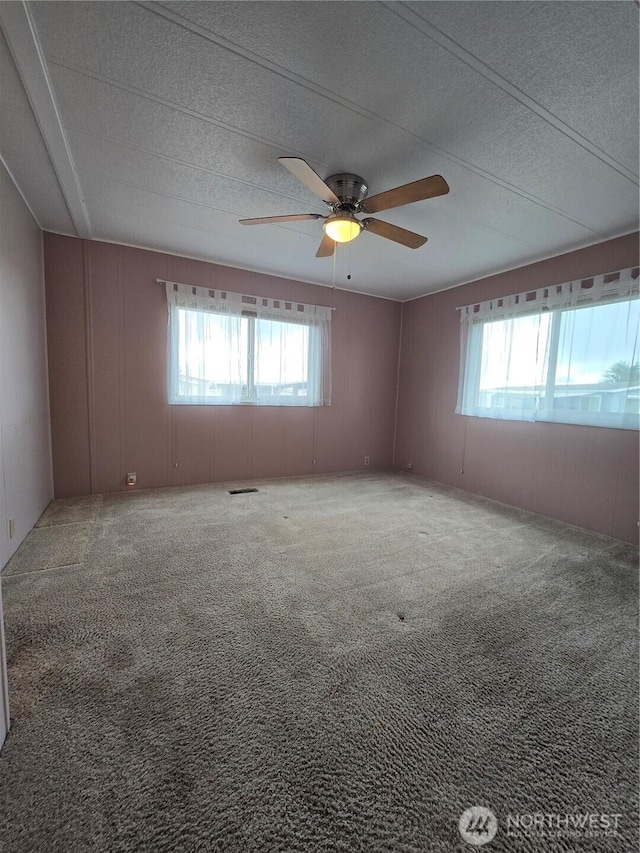 carpeted spare room featuring visible vents, a textured ceiling, and a ceiling fan