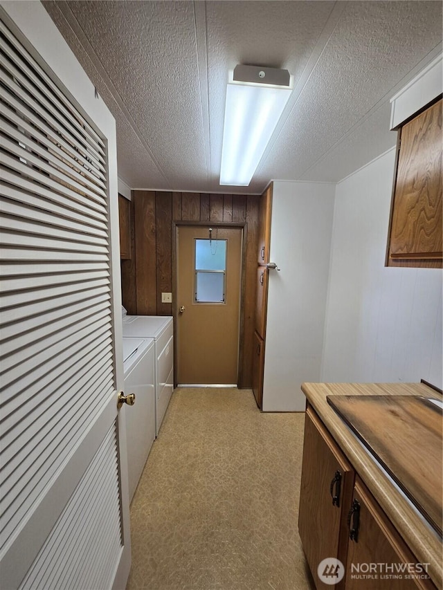 laundry area with washer and dryer, cabinet space, wood walls, and a textured ceiling