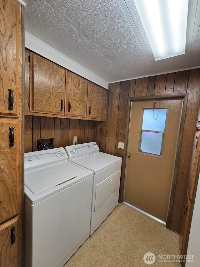 laundry area featuring a textured ceiling, wooden walls, cabinet space, and washing machine and clothes dryer