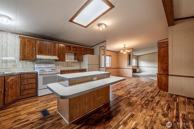 kitchen with under cabinet range hood, a center island, white appliances, an inviting chandelier, and wallpapered walls