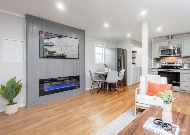 living room featuring light wood-style flooring, washer and dryer, recessed lighting, a large fireplace, and baseboards