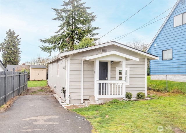 bungalow-style house featuring a storage shed, a front yard, fence, and an outbuilding