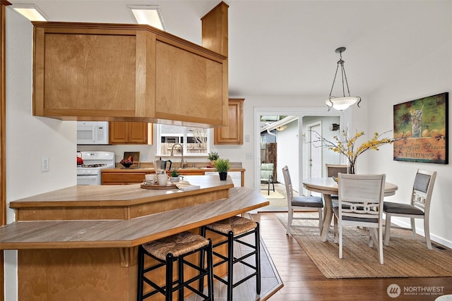 kitchen featuring dark wood-type flooring, a breakfast bar, pendant lighting, a sink, and white appliances