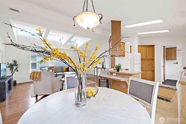 dining space with light wood finished floors, a skylight, and baseboards