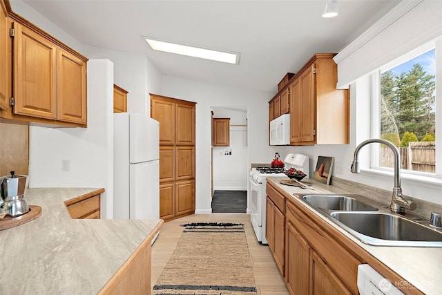 kitchen featuring white appliances, brown cabinetry, a sink, light countertops, and lofted ceiling with skylight