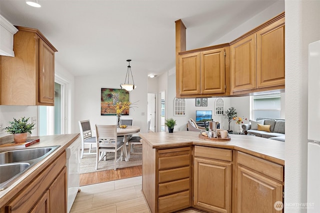 kitchen featuring a peninsula, white dishwasher, a sink, hanging light fixtures, and light countertops