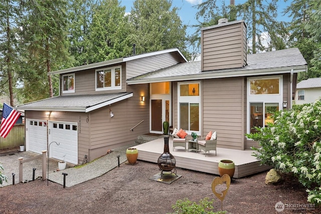 back of property featuring a deck, an attached garage, a shingled roof, and a chimney