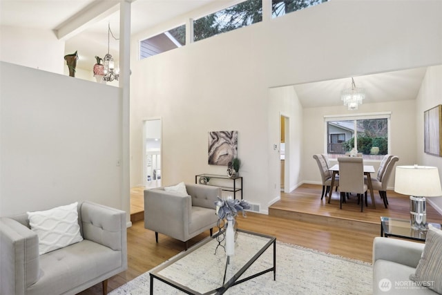 living area featuring visible vents, a notable chandelier, high vaulted ceiling, wood finished floors, and baseboards