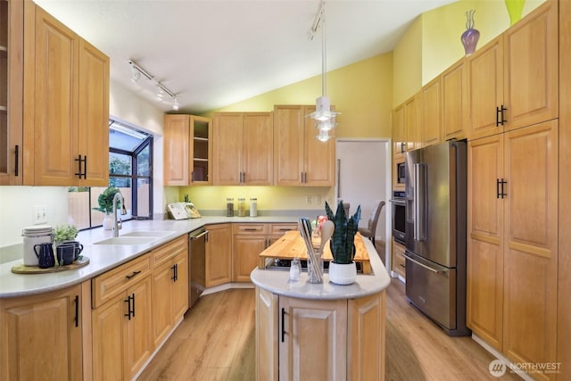 kitchen with a sink, light wood-style floors, appliances with stainless steel finishes, light countertops, and vaulted ceiling