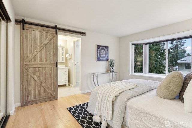 bedroom featuring connected bathroom, baseboards, light wood-type flooring, and a barn door