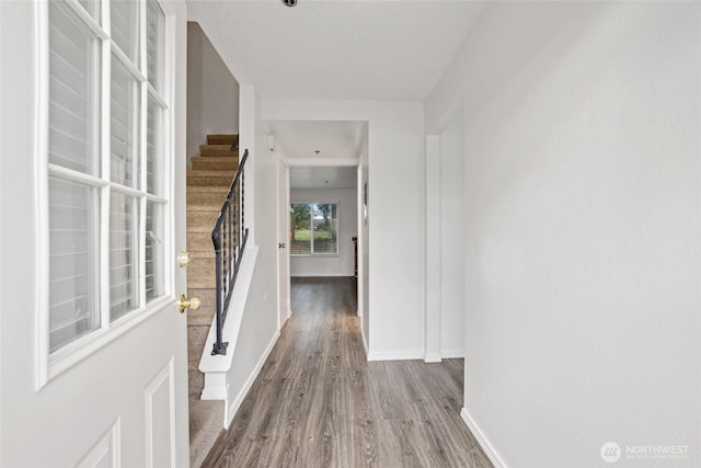 hallway featuring baseboards, wood finished floors, and stairs