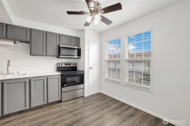 kitchen featuring a ceiling fan, dark wood-style floors, gray cabinets, a sink, and appliances with stainless steel finishes