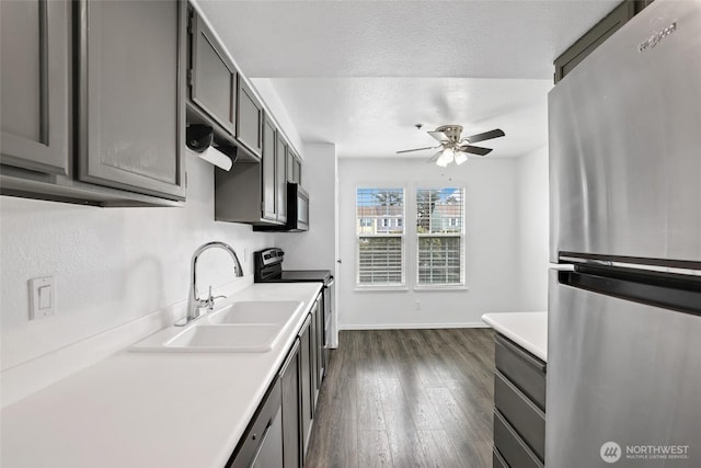 kitchen featuring gray cabinetry, dark wood-style floors, stainless steel appliances, a ceiling fan, and a sink