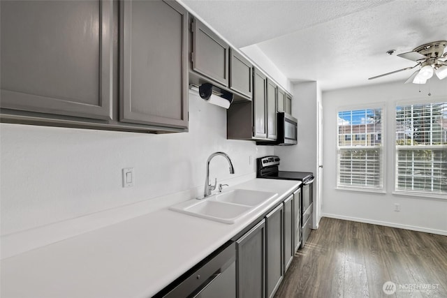 kitchen with a sink, dark wood-style floors, stainless steel appliances, light countertops, and ceiling fan