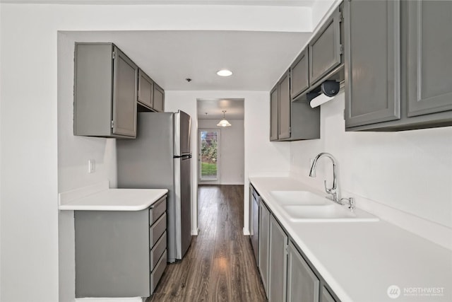 kitchen with gray cabinets, a sink, dark wood finished floors, freestanding refrigerator, and light countertops