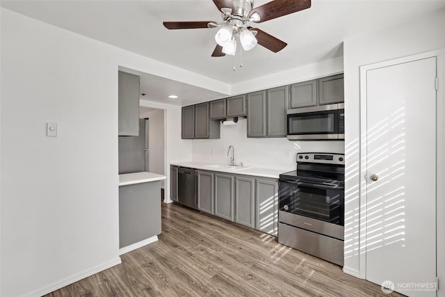 kitchen featuring gray cabinetry, light countertops, light wood-style flooring, appliances with stainless steel finishes, and a sink