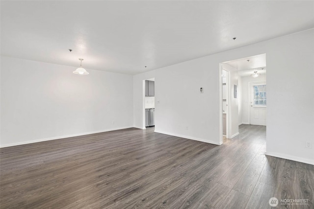 unfurnished living room with dark wood-type flooring and baseboards