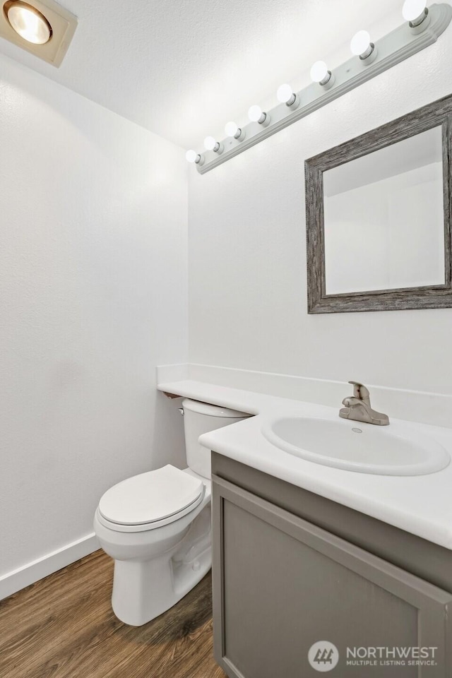 half bath with baseboards, toilet, wood finished floors, and vanity