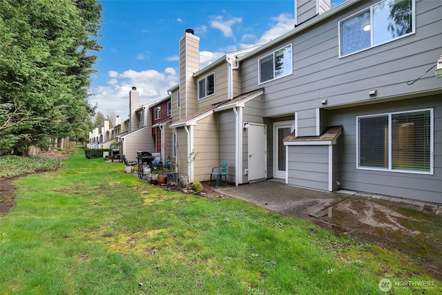 back of property with a yard, a chimney, and a patio area