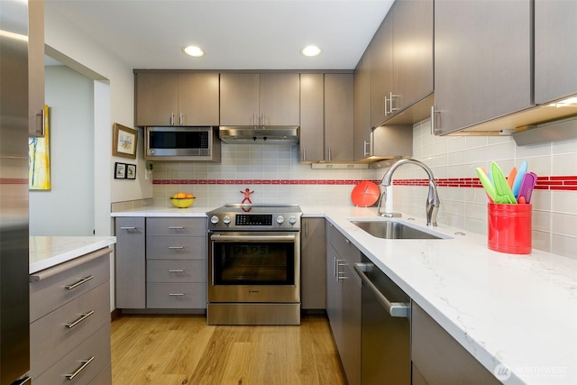 kitchen with gray cabinets, a sink, under cabinet range hood, stainless steel appliances, and light wood-style floors