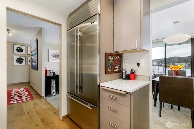 kitchen with light stone counters, baseboards, light wood finished floors, built in fridge, and decorative light fixtures