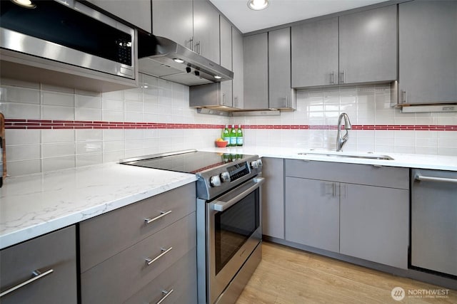 kitchen featuring gray cabinetry, appliances with stainless steel finishes, under cabinet range hood, and a sink