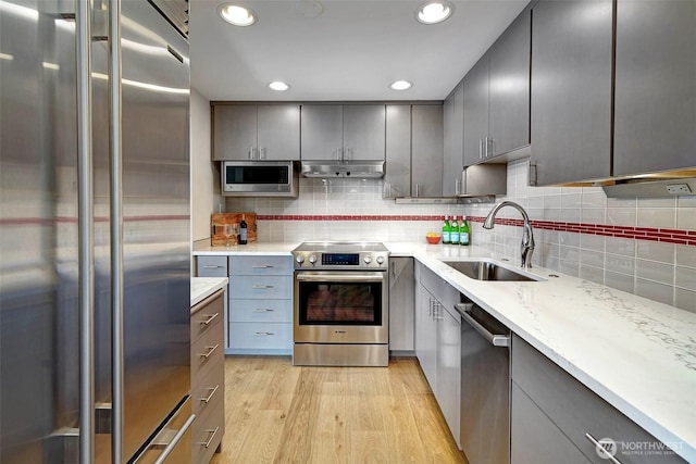 kitchen with under cabinet range hood, gray cabinets, appliances with stainless steel finishes, and a sink