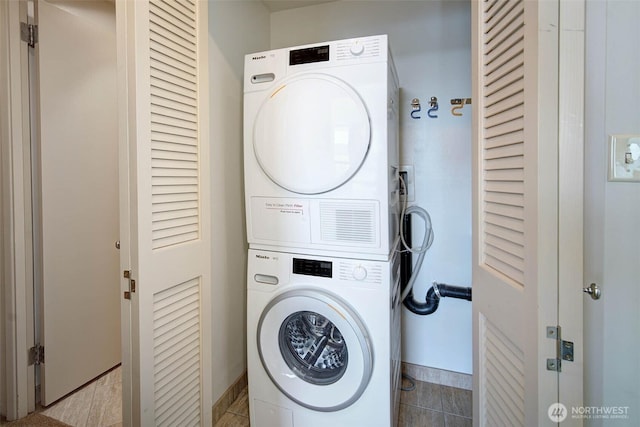 laundry room with baseboards, tile patterned floors, stacked washer and dryer, and laundry area