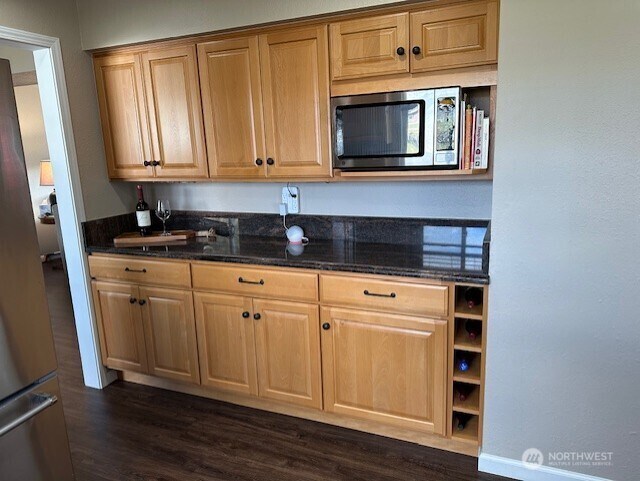 kitchen featuring stainless steel microwave, dark wood finished floors, and dark stone counters