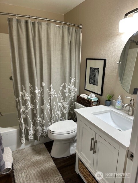 bathroom featuring toilet, shower / tub combo with curtain, a textured wall, wood finished floors, and vanity