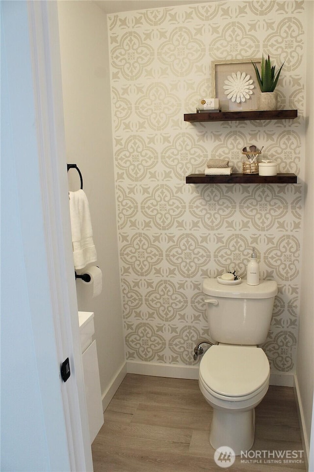 bathroom featuring baseboards, toilet, wood finished floors, and wallpapered walls