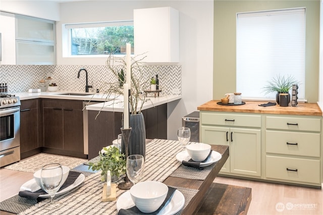 kitchen featuring a sink, light wood-style floors, stainless steel stove, butcher block counters, and decorative backsplash