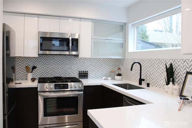 kitchen with modern cabinets, a sink, white cabinetry, appliances with stainless steel finishes, and light countertops