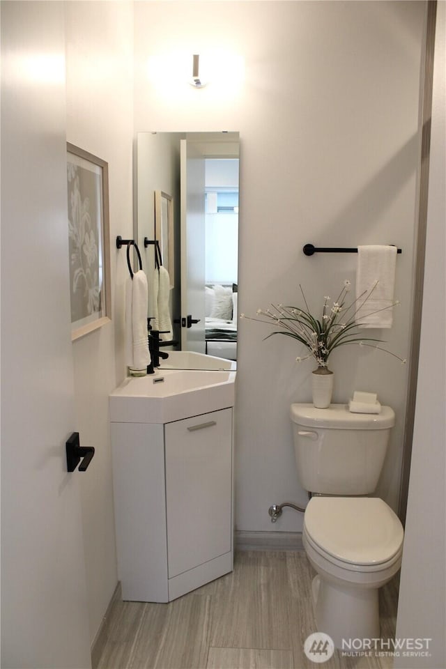 half bath with baseboards, toilet, and vanity