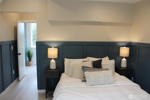 bedroom featuring wood finished floors, wainscoting, and a decorative wall