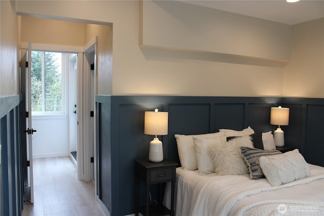 bedroom with a decorative wall, light wood finished floors, and wainscoting