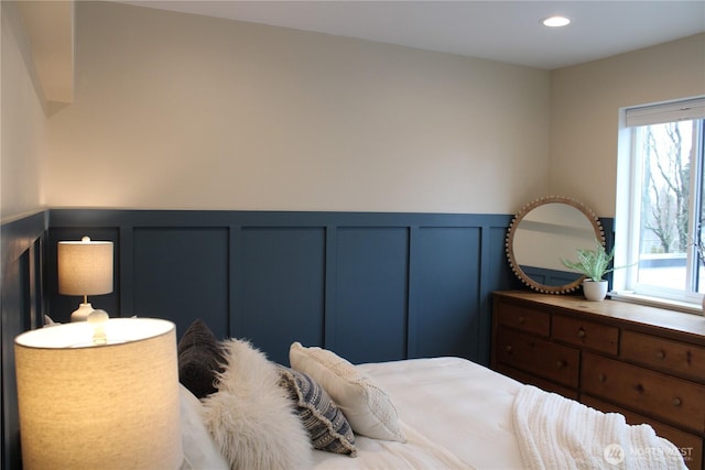 bedroom featuring recessed lighting, wainscoting, and a decorative wall