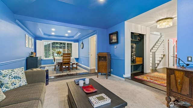 carpeted living area featuring a notable chandelier, recessed lighting, stairway, baseboards, and a raised ceiling