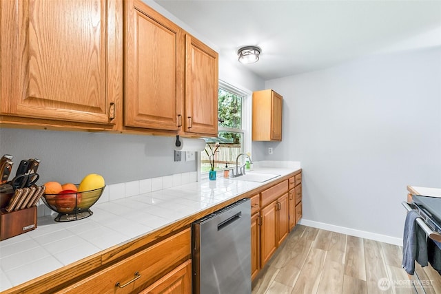 kitchen featuring a sink, tile countertops, light wood-style floors, appliances with stainless steel finishes, and baseboards