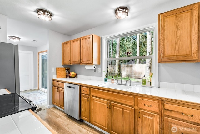 kitchen featuring tile counters, brown cabinets, appliances with stainless steel finishes, light wood-style floors, and a sink