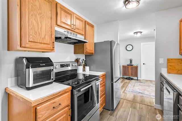 kitchen featuring tile counters, under cabinet range hood, a toaster, light wood-type flooring, and electric range