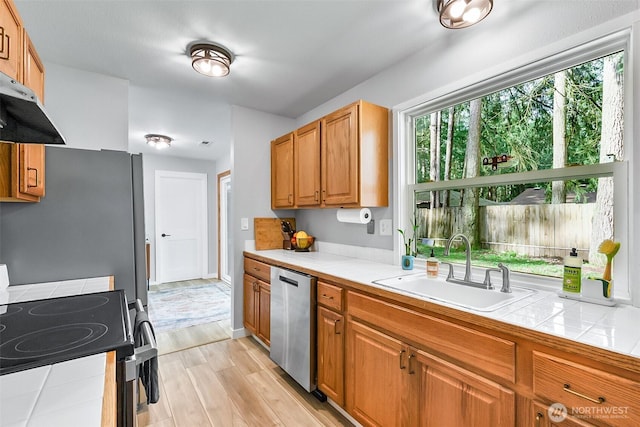 kitchen with tile countertops, light wood-style floors, appliances with stainless steel finishes, and a sink