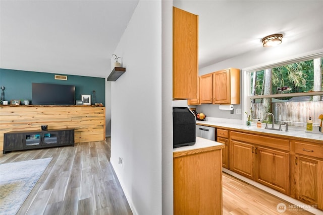 kitchen featuring a sink, light wood-type flooring, stainless steel dishwasher, and light countertops